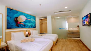 A hotel room with two beds, a large painting, a wardrobe, a bathroom with a sink and mirror, and a TV on the wall.