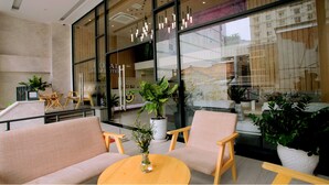 A modern lobby with seating, a potted plant, and a view of the city through large windows.