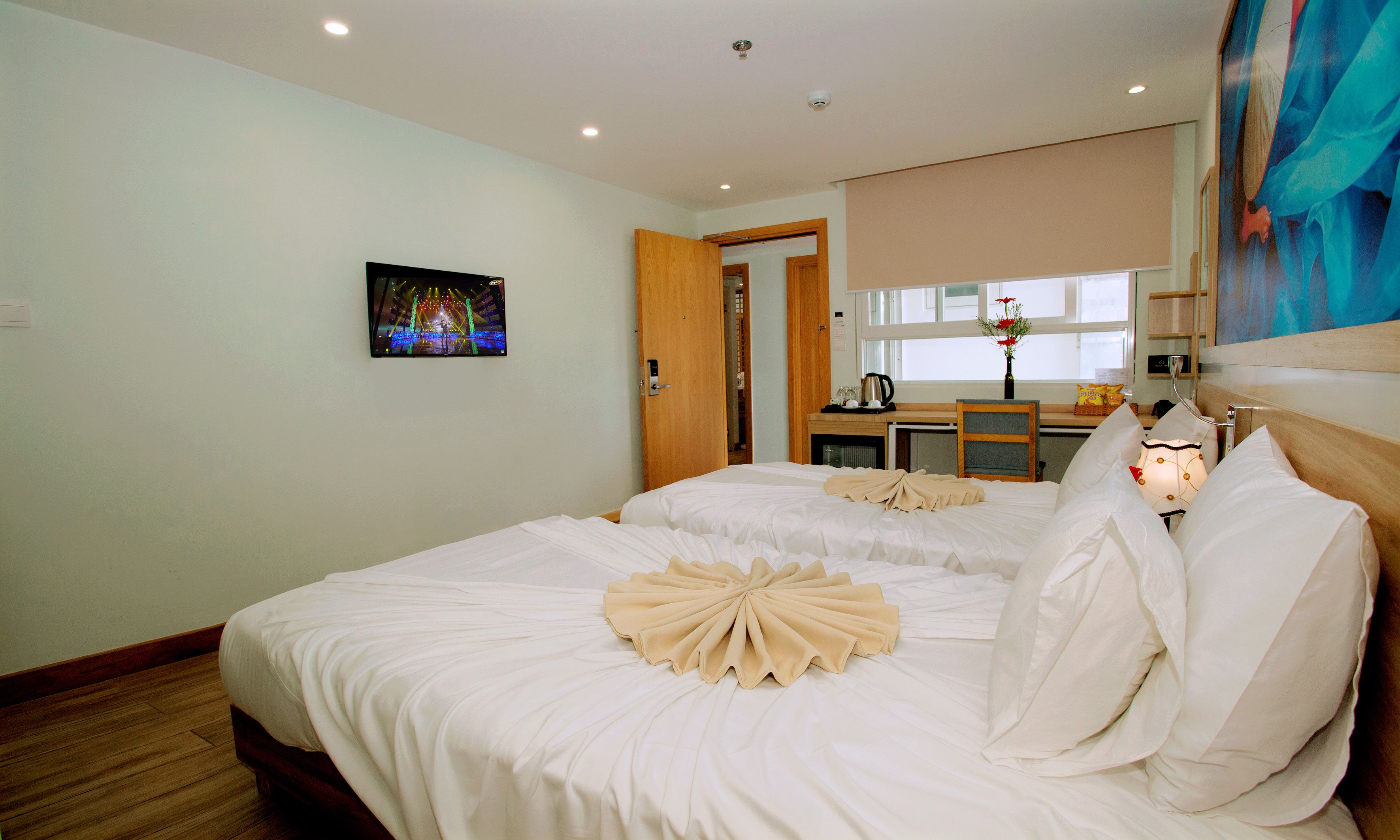 A hotel room with two beds, a painting on the wall, a window with a view, and a kitchenette area.
