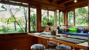 Un interno in legno con ampie finestre, un angolo cottura e sgabelli colorati.