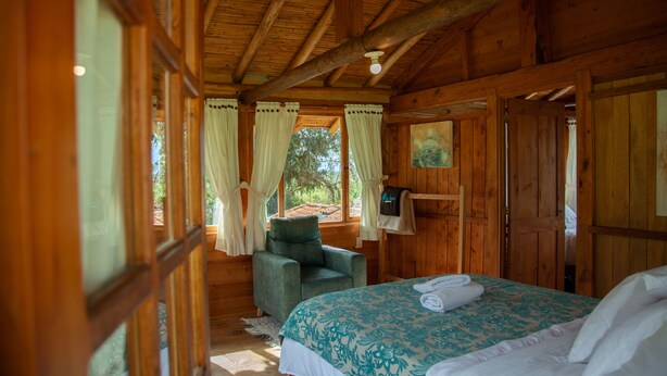Una camera in una baita di legno, con un letto, una sedia e una finestra con tende.