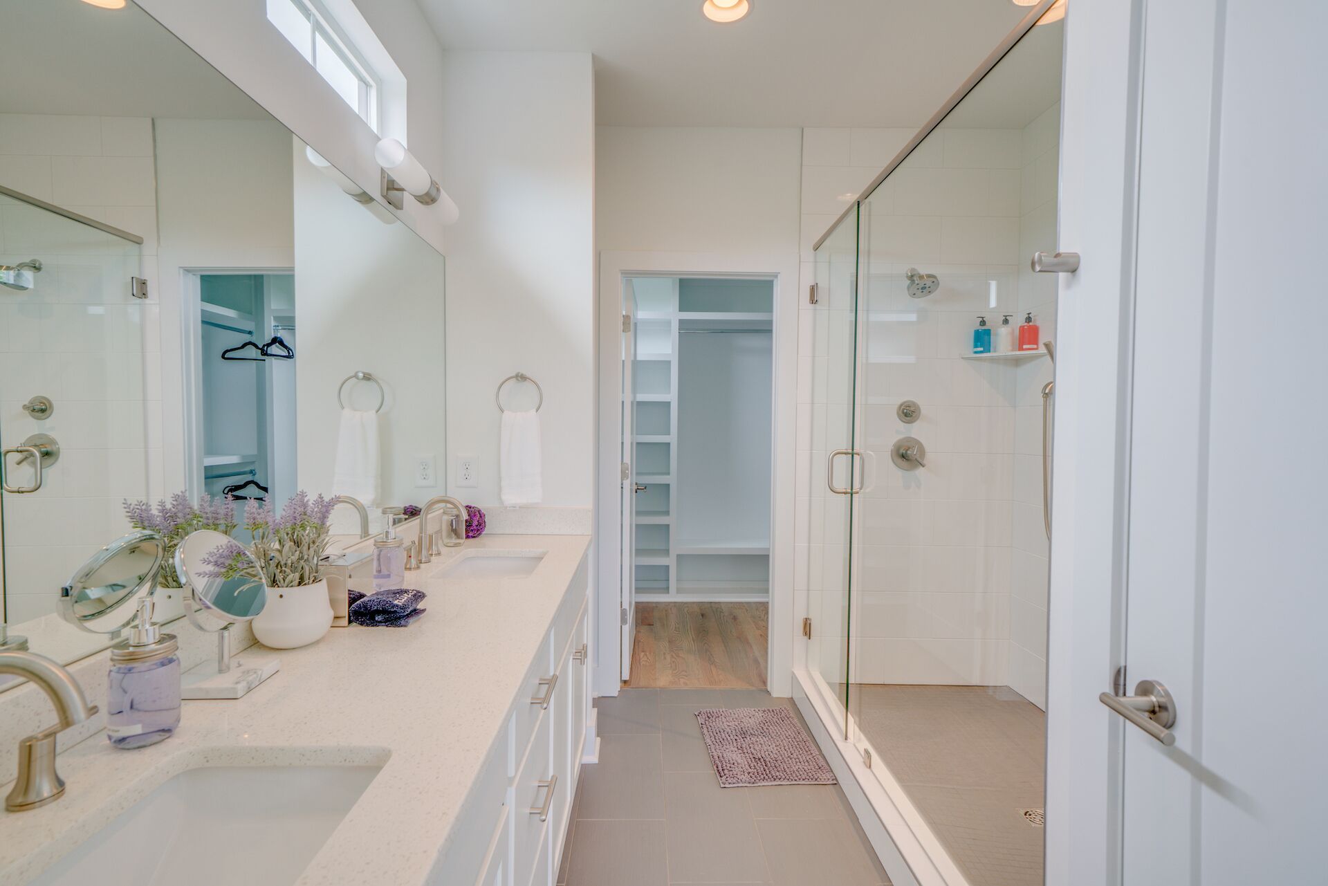 Een moderne badkamer met een grote spiegel, twee wastafels, een douche en een inloopkast.