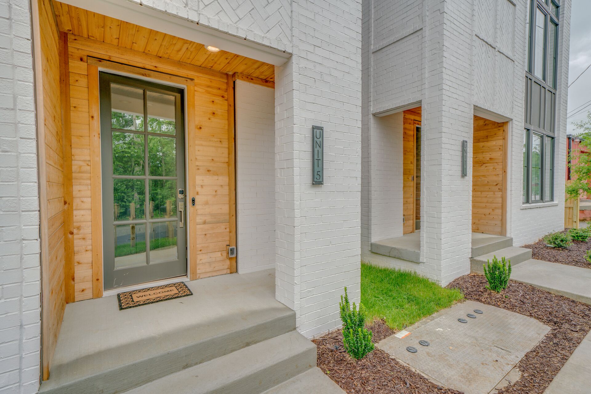 A modern building with a white brick exterior, wooden door, and a welcome mat.