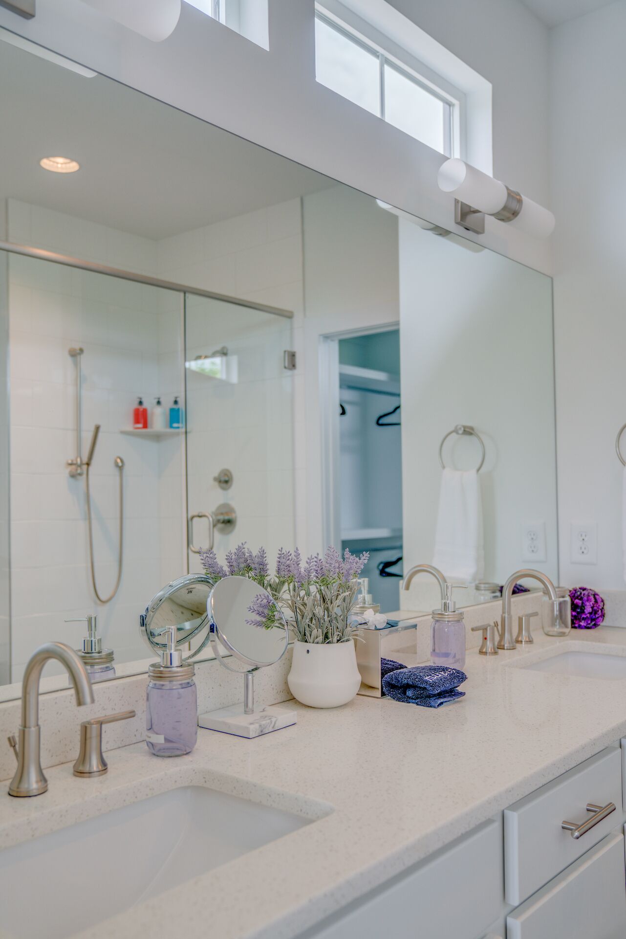 A modern bathroom with a large mirror, two sinks, and a shower.