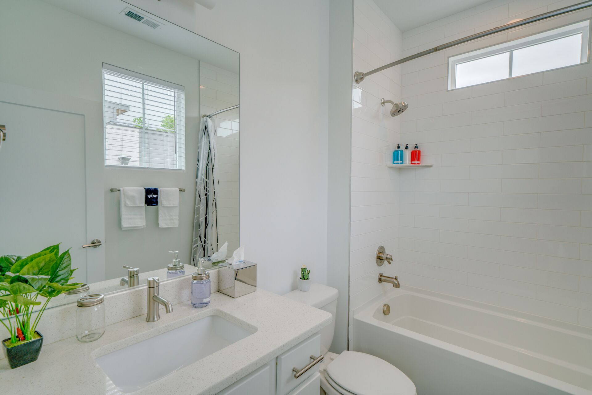 A modern bathroom with a white sink, a toilet, and a bathtub. There are two bottles of soap on a shelf above the bathtub.