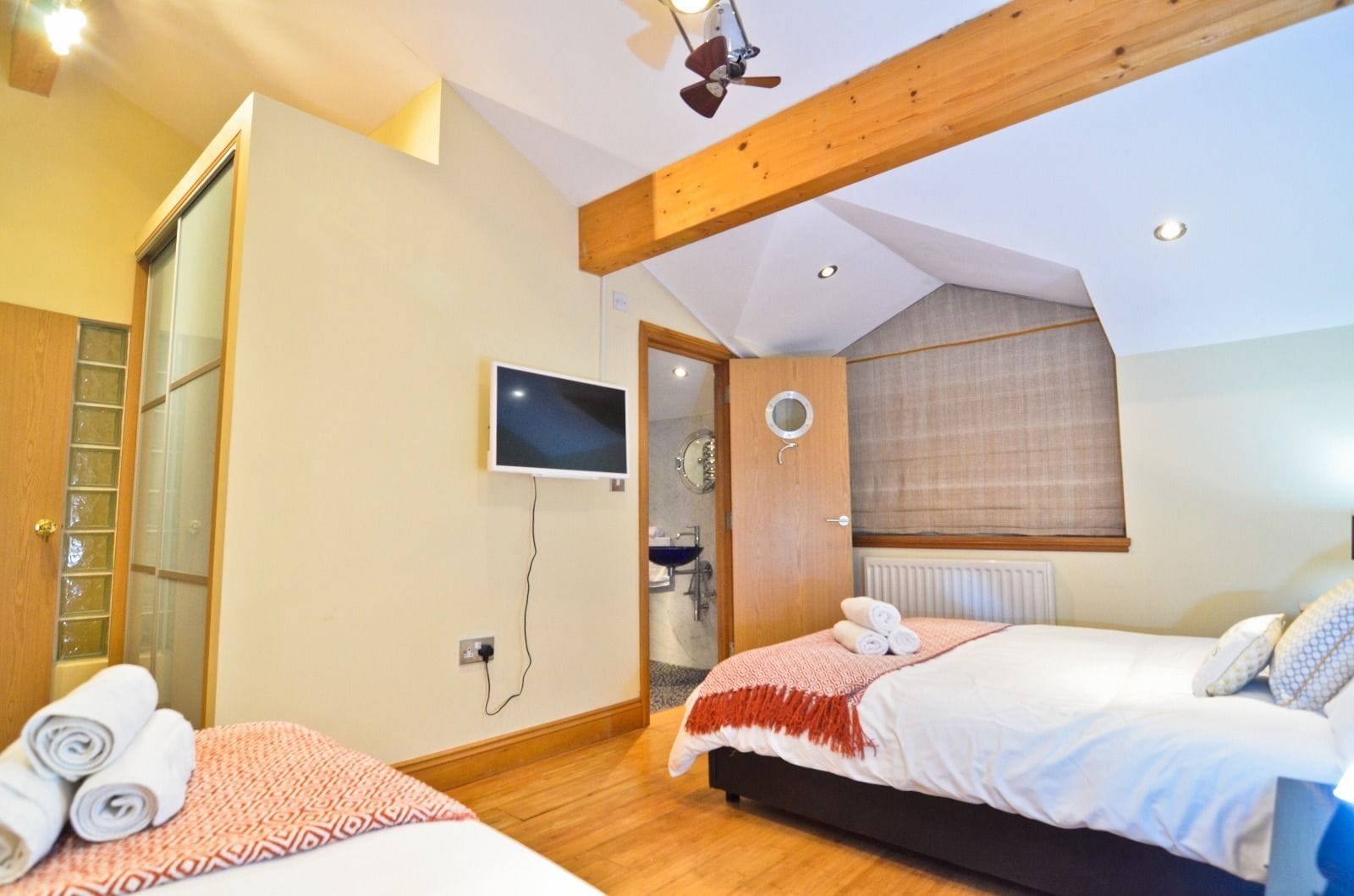 Une chambre à coucher avec un lit, une télévision, un miroir et une salle de bain visible à travers une porte ouverte.