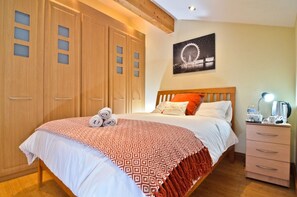 A hotel room with a large bed, a nightstand with a lamp, a wooden wardrobe, and a wall-mounted picture of a Ferris wheel.