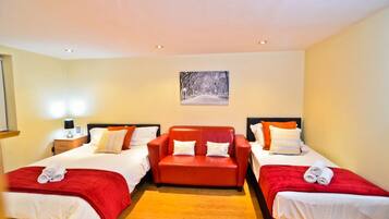 A hotel room with two single beds and a sofa bed, each with red bedding and pillows. There is a painting on the wall above the sofa bed.