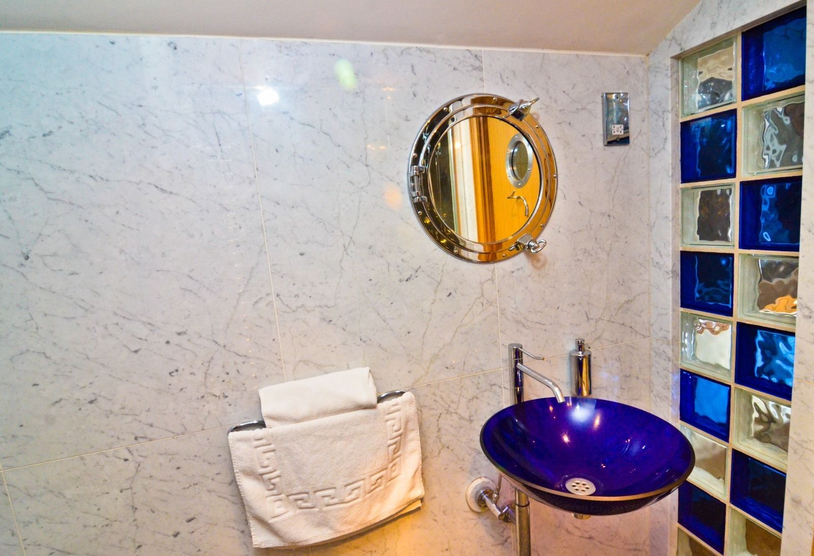 Une salle de bain avec un mur en marbre, un miroir rond, un lavabo bleu et un porte-serviettes.