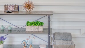 Un salon avec un téléviseur fixé au mur, une console en bois agrémentée d’objets décoratifs, un fauteuil gris et un panier.