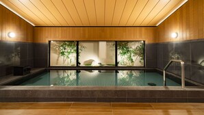 Een wellnessruimte met een groot binnenzwembad, houten plafond en betegelde muren.