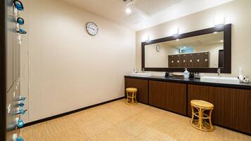 Un baño con un espejo grande, suelo de madera, dos taburetes y un reloj en la pared.