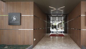 Een moderne hotelentree met een houten gevel, een receptiebalie en een rode loper die naar de lobby leidt.