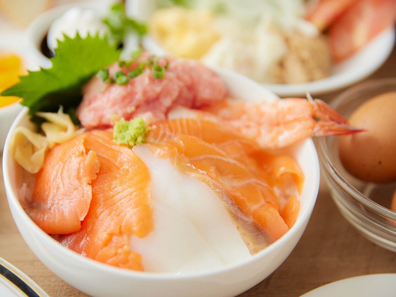 A bowl of sashimi with salmon and shrimp, garnished with green onions and wasabi.