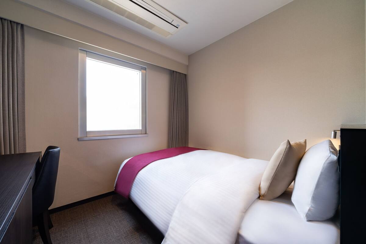 A hotel room with a bed, a desk, and a window.