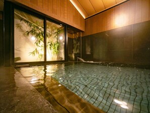 Une piscine intérieure avec un sol carrelé, des murs en bois et de grandes fenêtres ornées de plantes en bambou.