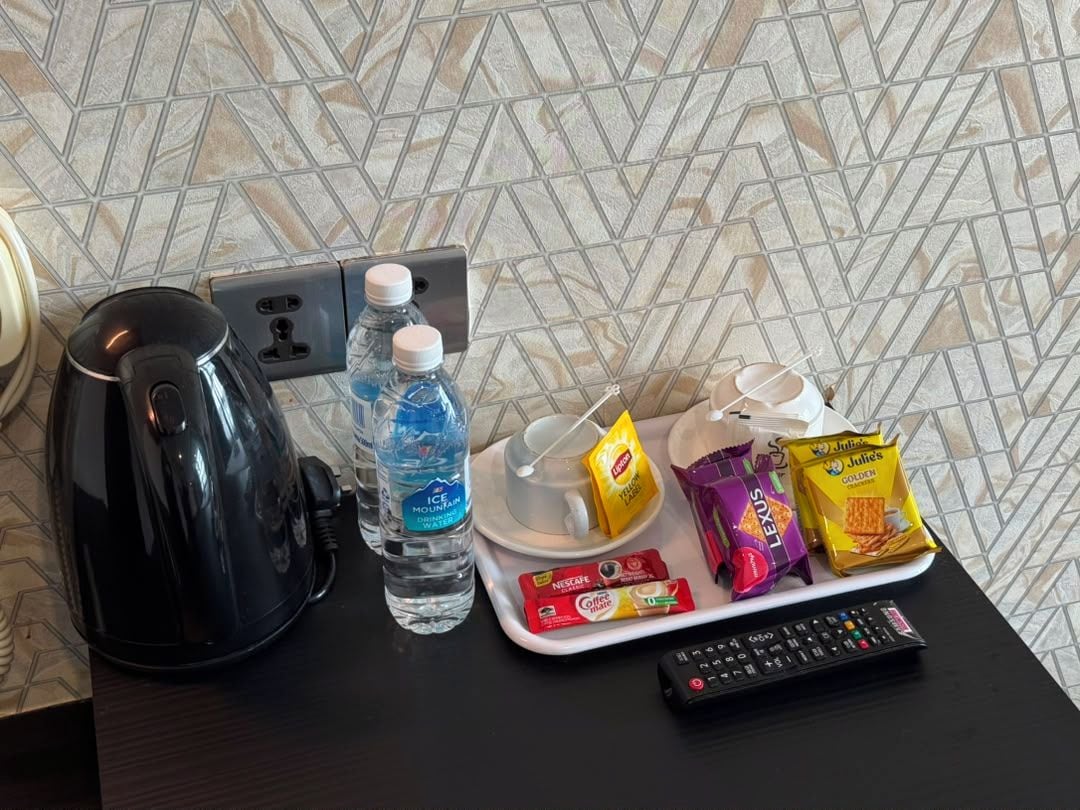 A kitchen area with a kettle, water bottle, coffee maker, tray with snacks, and a remote control.