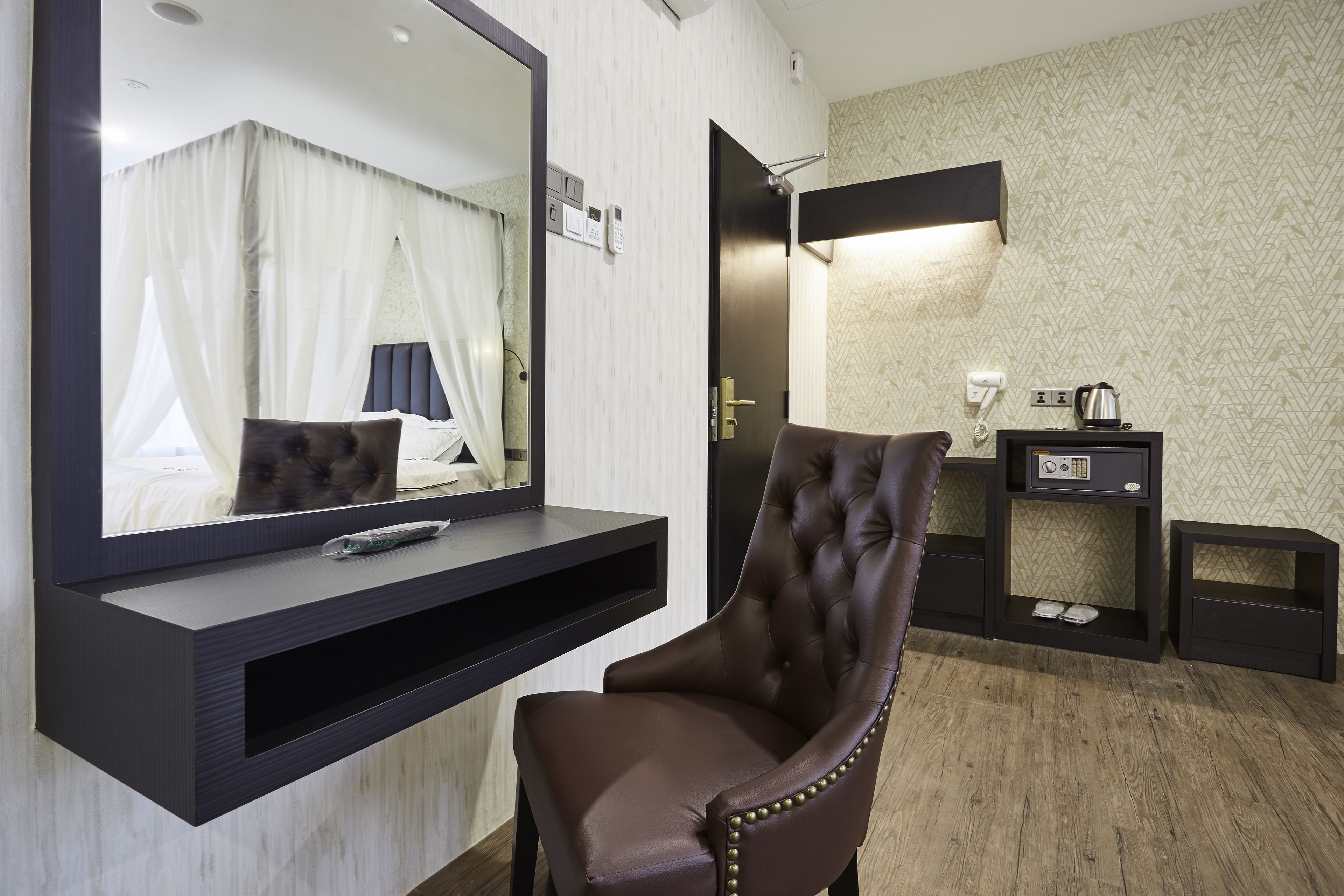 Una habitación de hotel moderna con un espejo grande, un sillón de cuero marrón, una mesita de noche y un televisor montado en la pared.