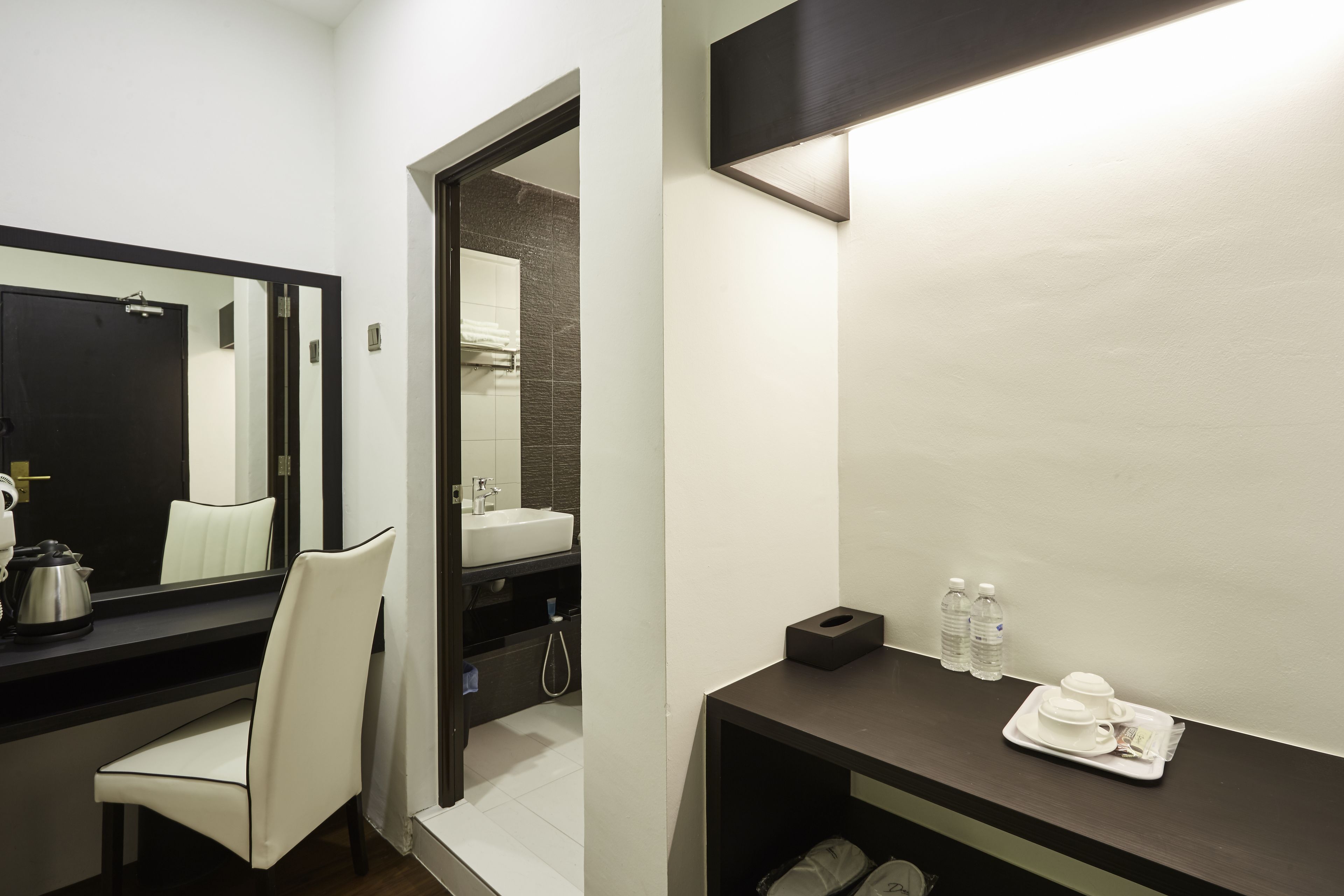 Un baño moderno con un espejo grande, un lavamanos, una silla y una bandeja con artículos de aseo.