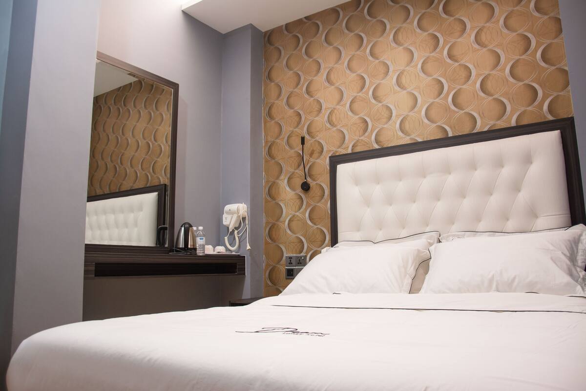 A hotel room with a large bed, a bedside table with a phone and a lamp, and a wall with a circular pattern.