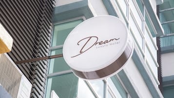 A sign for Dream Luxury Hotel with a modern building facade in the background.