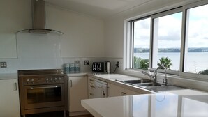 Une cuisine moderne dotée d’un grand îlot central, d’appareils électroménagers en acier inoxydable et offrant une vue sur l’eau grâce à une grande fenêtre.