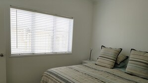 Une chambre à coucher avec un lit, une table de chevet, une lampe et une fenêtre avec des stores.