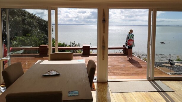 Une pièce moderne avec une grande table et des chaises en bois, une porte vitrée donnant sur un balcon avec vue sur la mer.