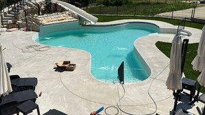 A swimming pool with a slide, lounge chairs, and umbrellas.