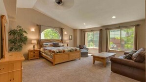 A bedroom with a bed, a wooden dresser, a nightstand, a coffee table, a sofa, and two windows with curtains.