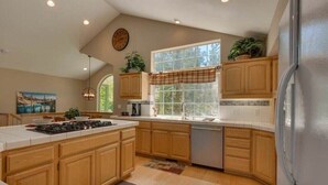 A kitchen with wooden cabinets, a central island, a window with a plaid valance, and a clock on the wall.