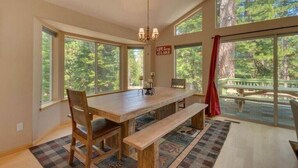 A dining area with a wooden table, benches, and large windows offering a view of the outdoors.