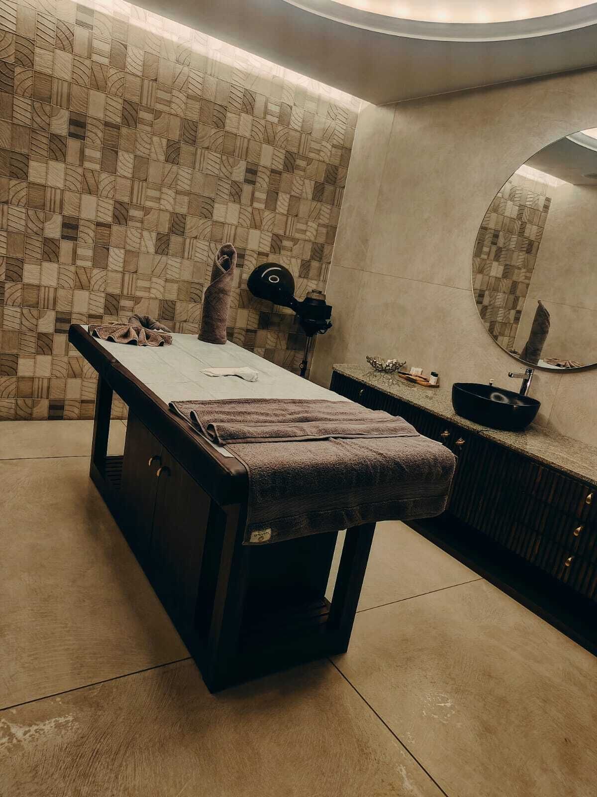 A spa room with a massage table, a towel, a massage chair, a small table with a bowl, and a mirror on the wall.