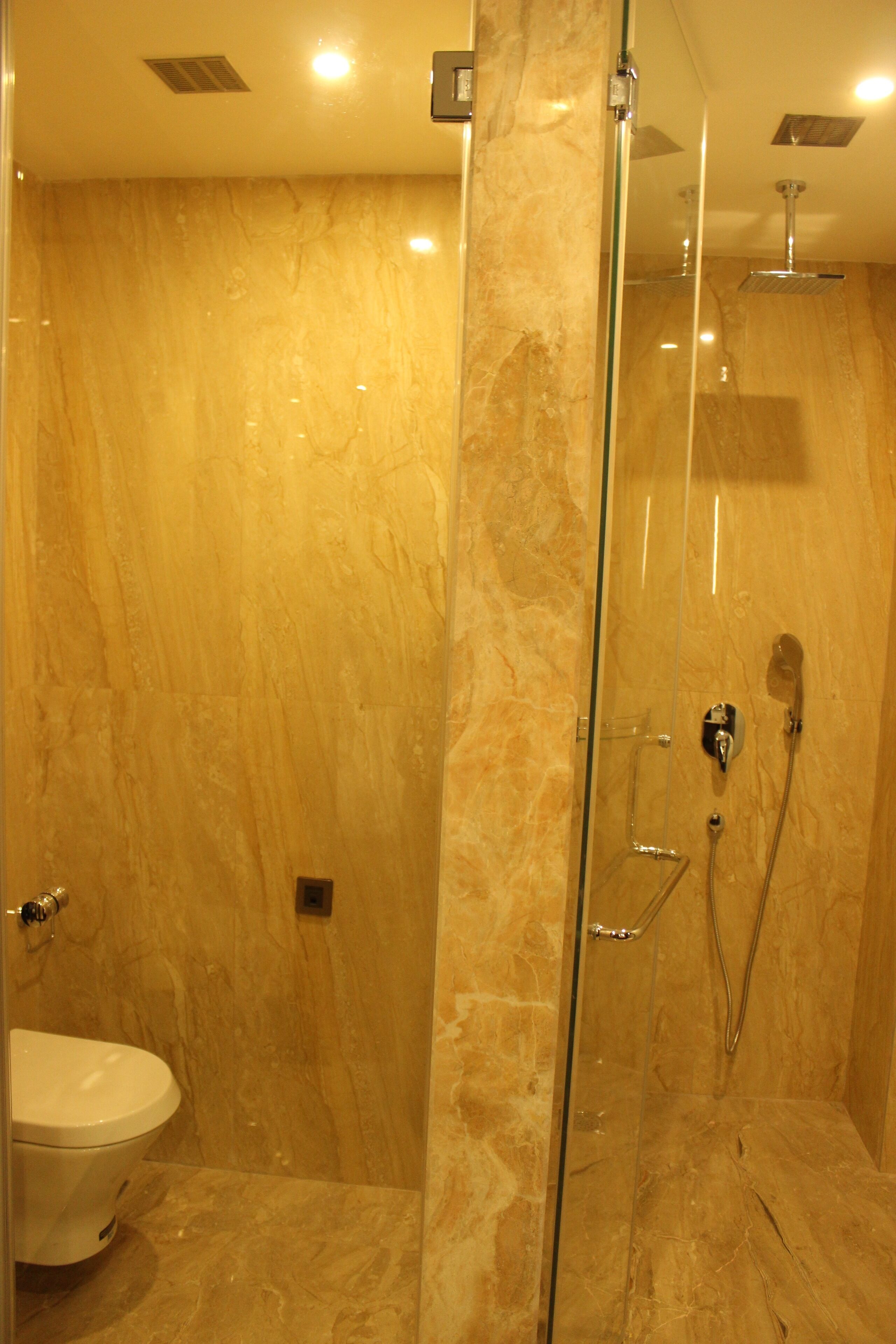 A modern bathroom with a glass-enclosed shower, marble walls, and a white toilet.