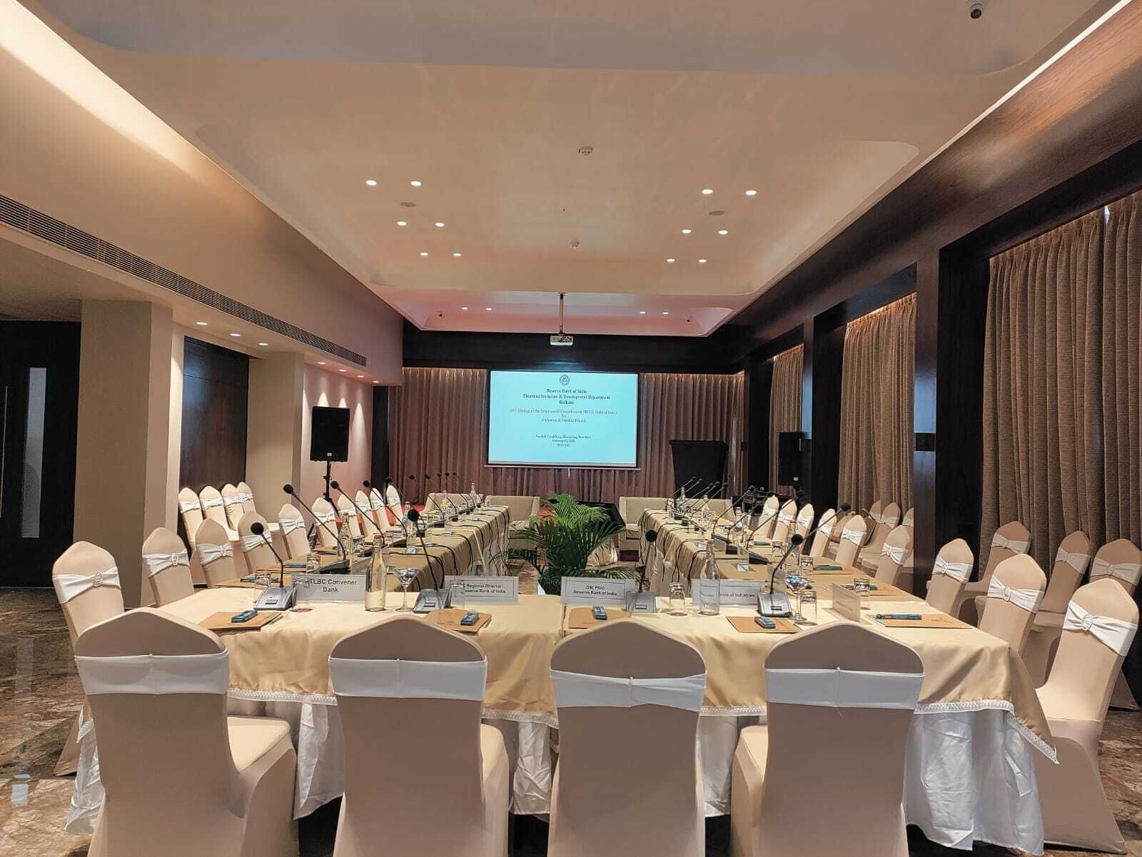 Una sala de conferencias con una larga mesa, sillas y una pantalla para proyector.
