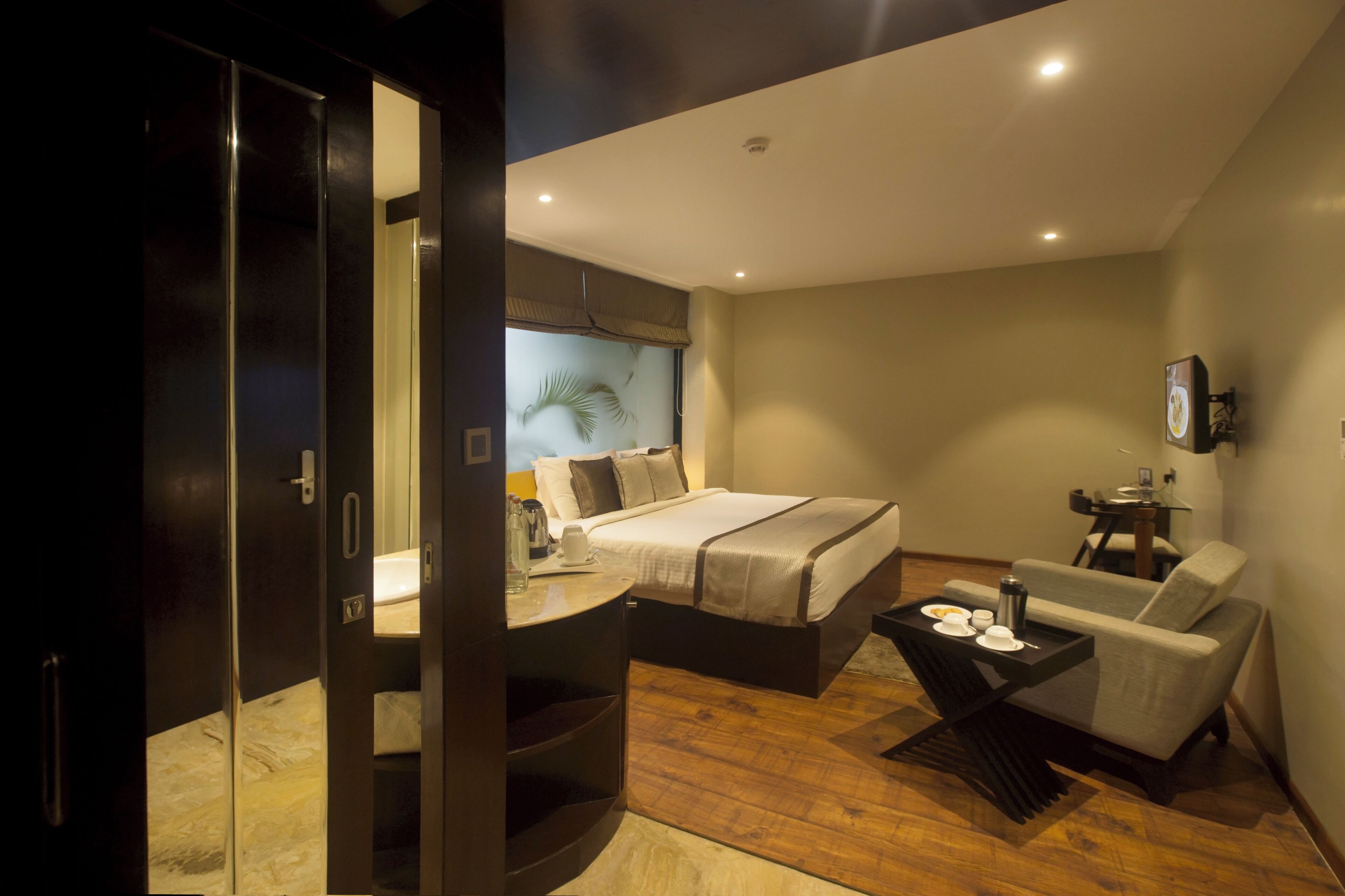 Ein modernes Hotelzimmer mit Bett, Sofa, kleinem Tisch mit Tablett und einer in Glaswänden gefassten Dusche.