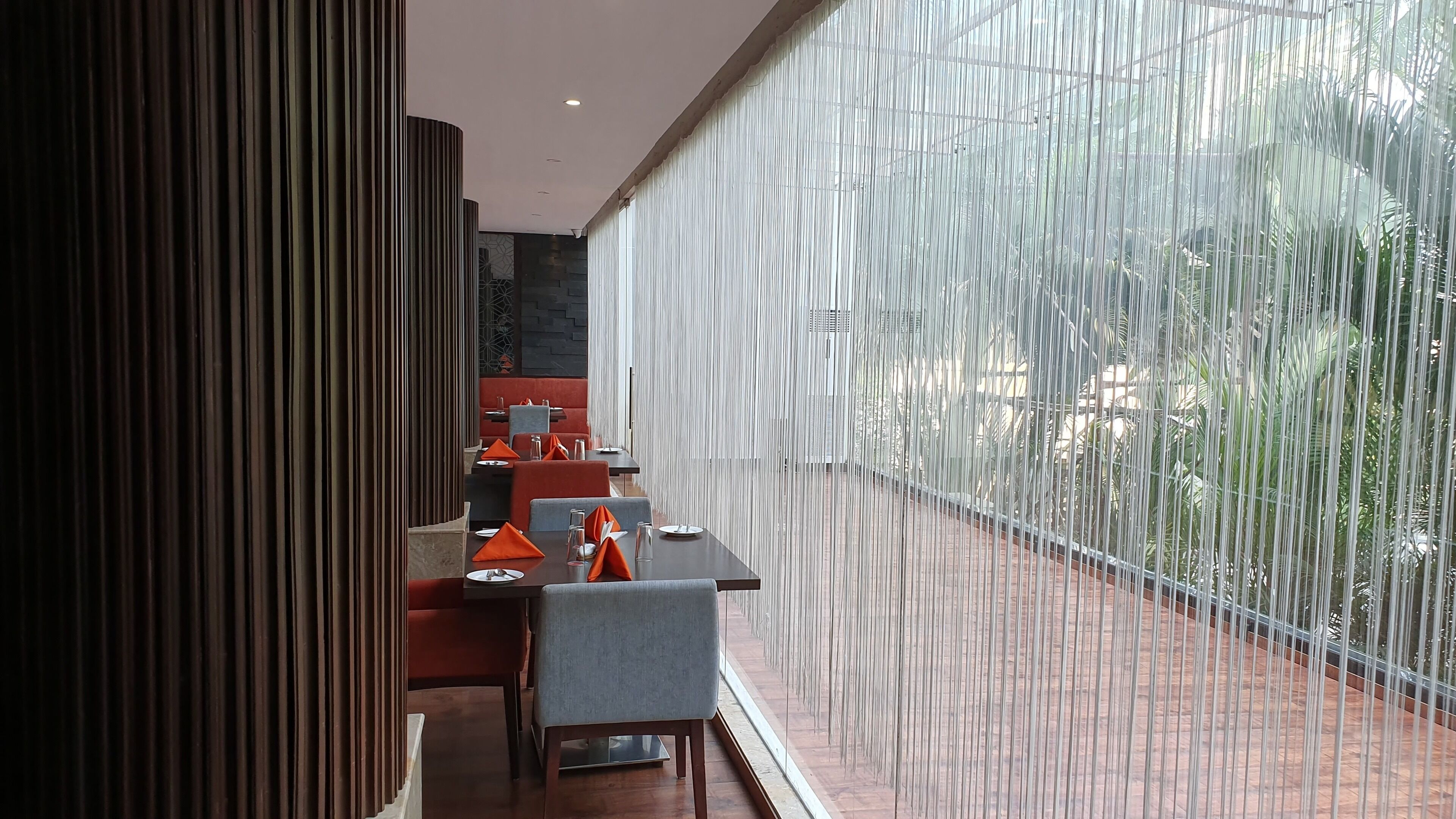 A modern restaurant with a long dining area, red and grey seating, and a view through a vertical glass partition.