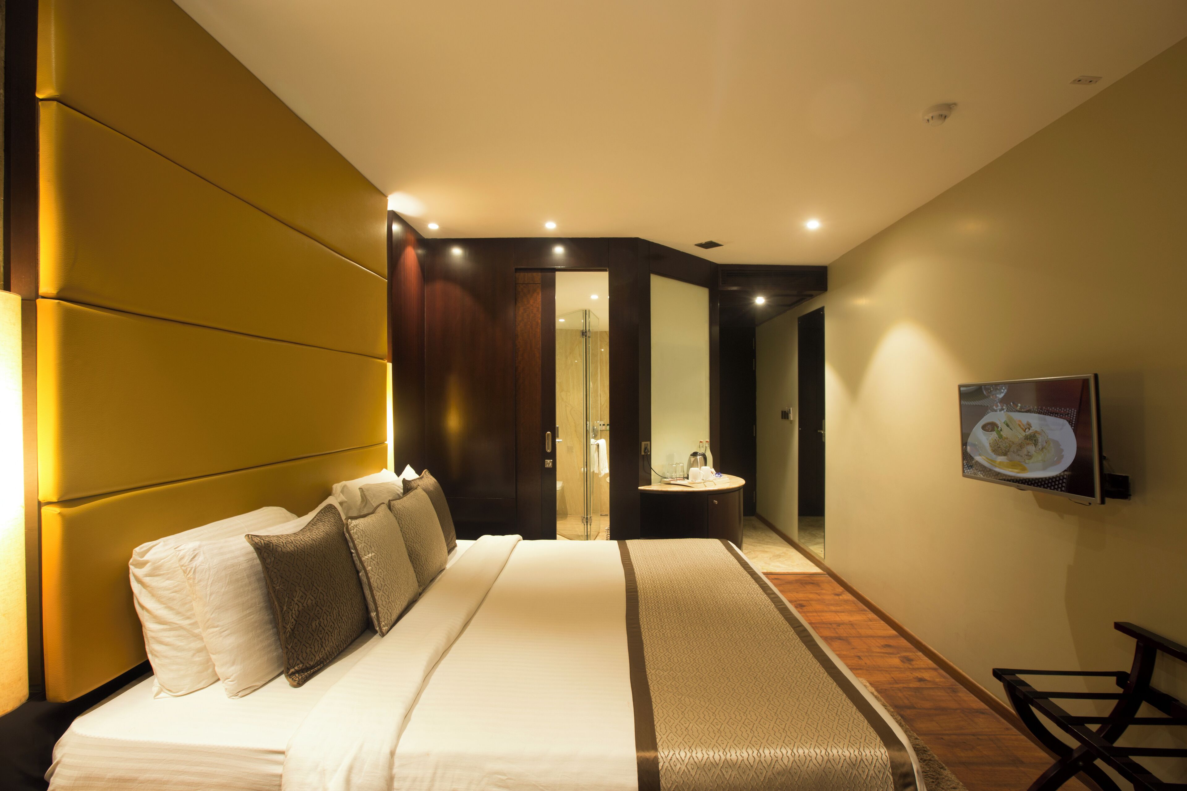 Une chambre d’hôtel moderne avec un grand lit, une table de chevet, un miroir et un téléviseur fixé au mur.