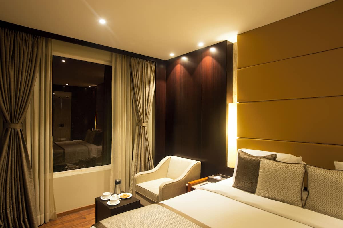 A hotel room with a large bed, a sitting area with a chair, a small table with cups and a plate, and a window with curtains.