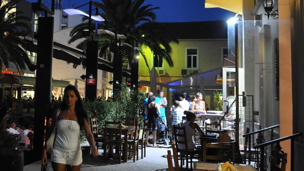 An outdoor dining area with tables and chairs, palm trees, and a building in the background. - Lovely apartments Marmont with balconies in the heart of Split (Split)