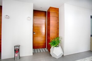 A modern entrance with a wooden door, a metal trash bin, and a potted plant.