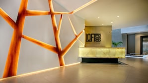 Uma área de recepção moderna com uma parede de detalhes em madeira geométrica, um balcão de atendimento e uma planta.