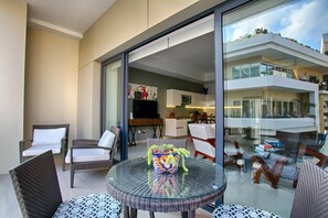 A modern living area with a glass table, wicker chairs, a sofa, and a kitchen in the background.