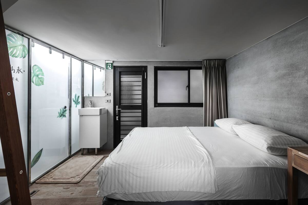 A bedroom with a bed, a bedside table, a wardrobe, and a window with curtains.