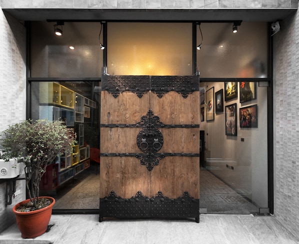 A wooden door with metal accents, a potted plant, and framed pictures on the wall.