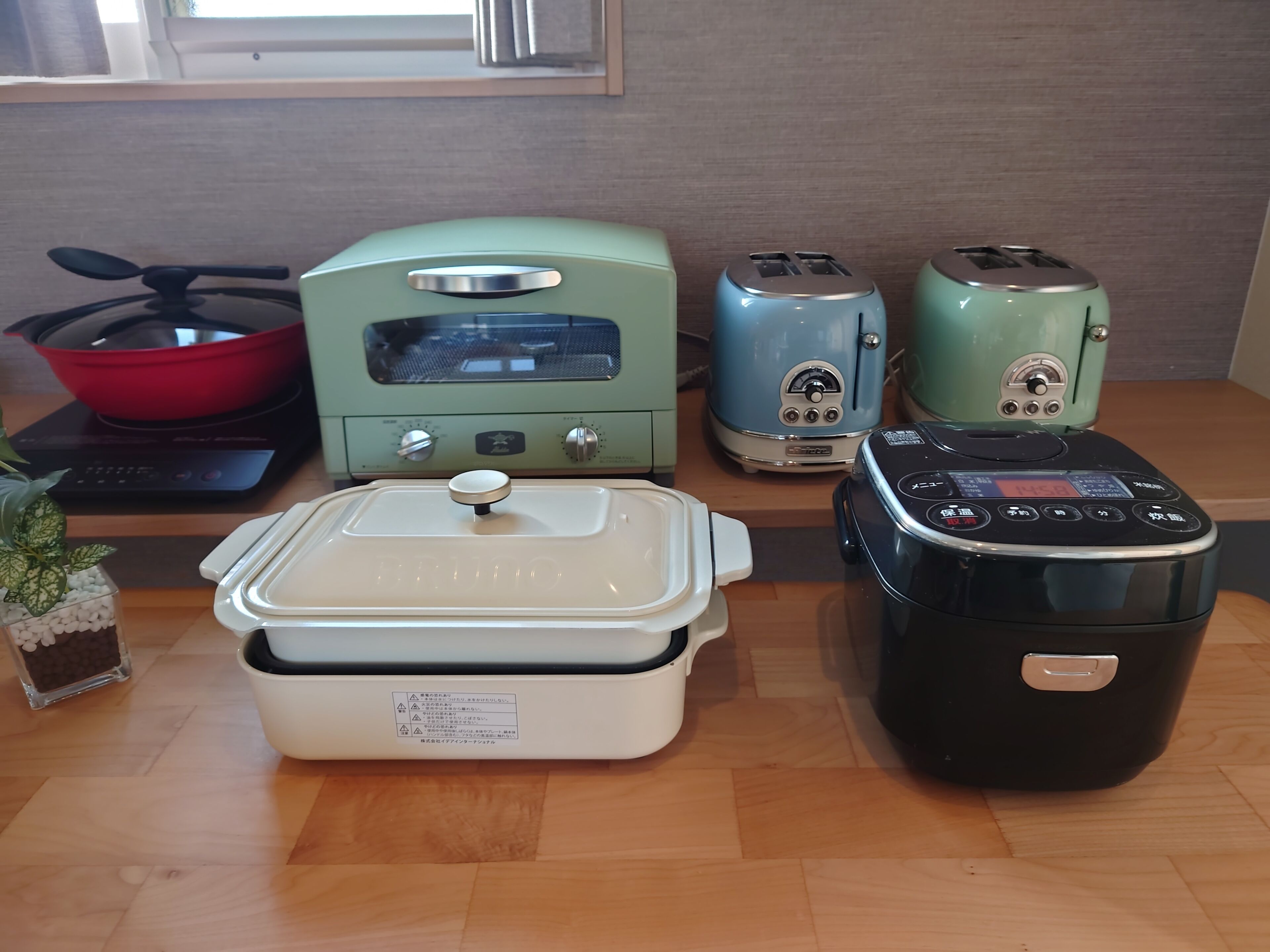 A kitchen with a microwave, toaster, rice cooker, and a pot on the stove.