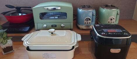 A kitchen with a microwave, toaster, rice cooker, and a pot on the stove.