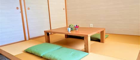 A tatami mat room with a low wooden table, cushions, and a small plant.