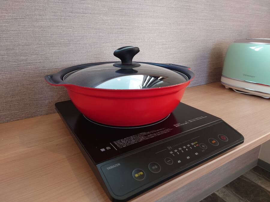 A red pot on a black electric stove with a digital control panel.