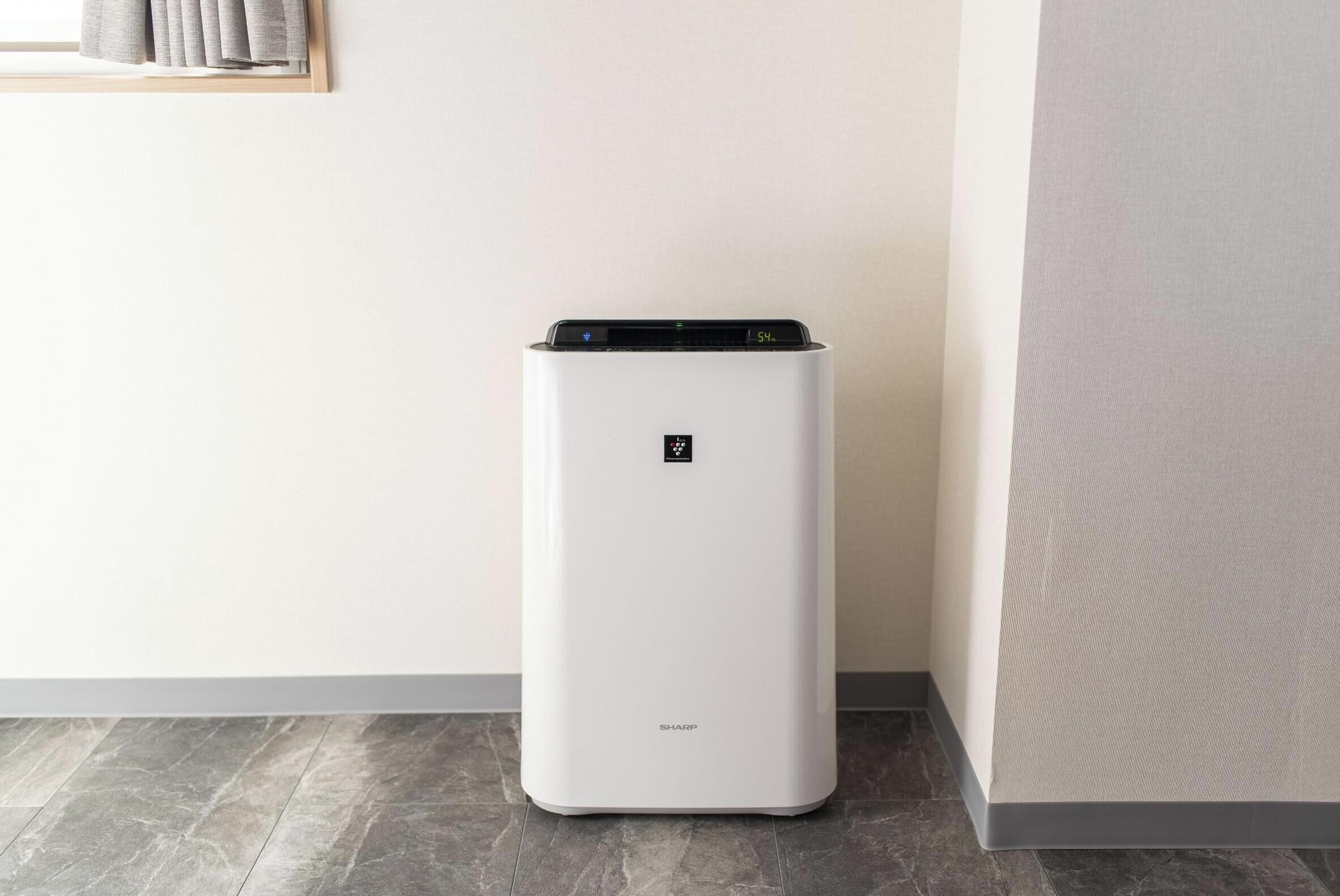 A white air purifier with a digital display, standing on a tiled floor.